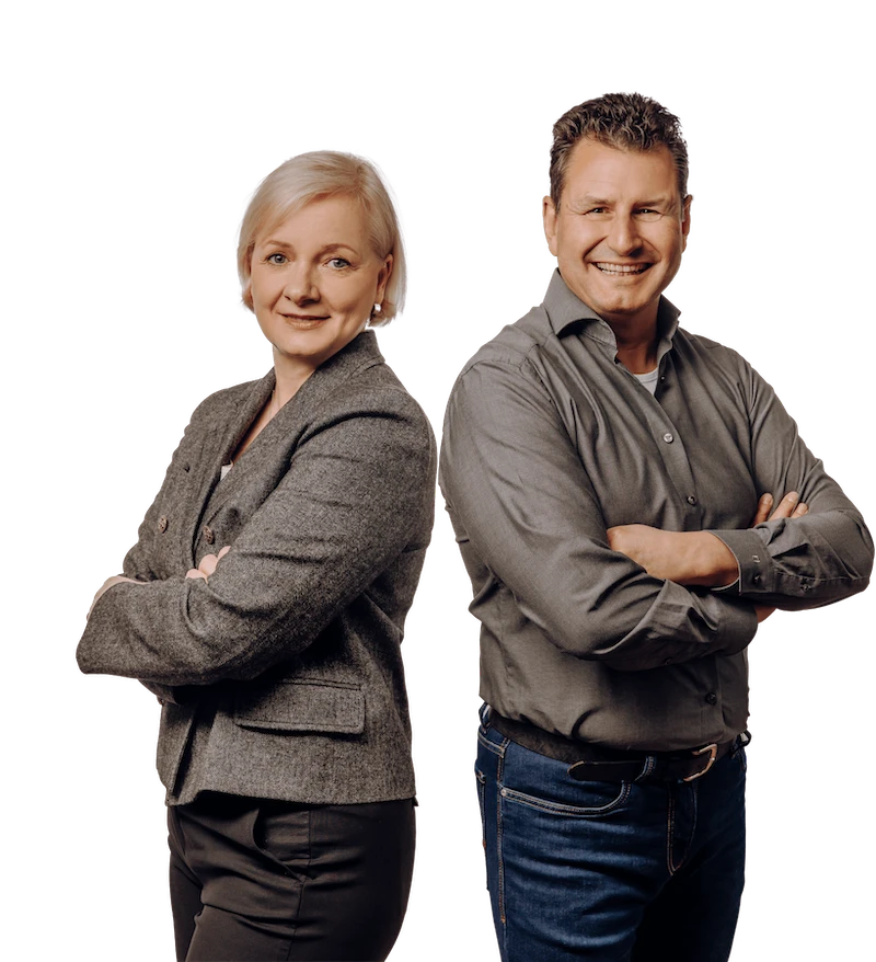 Zwei Personen stehen mit verschränkten Armen Rücken an Rücken, die Frau trägt einen blauen Blazer und der Mann ein graues Hemd.